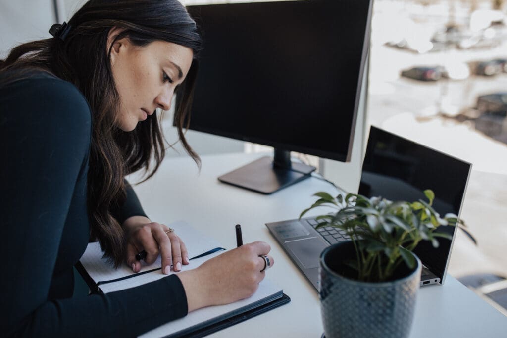 Woman writing in notebook at desk.