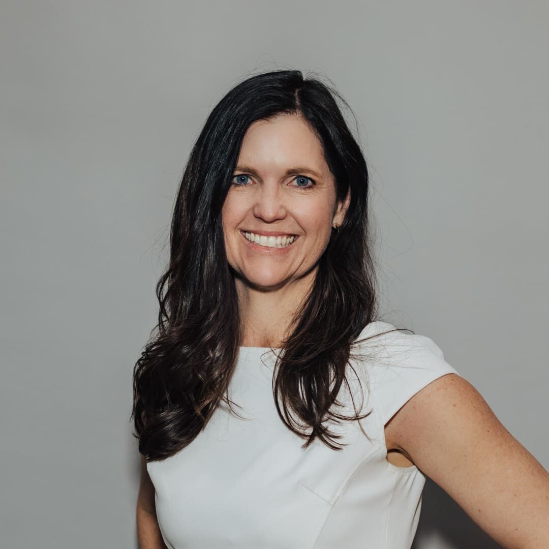 Woman smiling in white dress against gray wall.