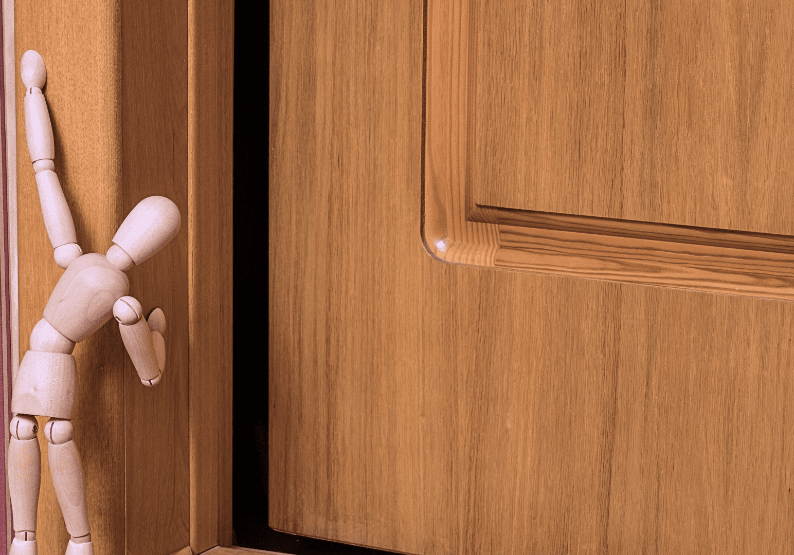 Wooden mannequin leaning against door frame.