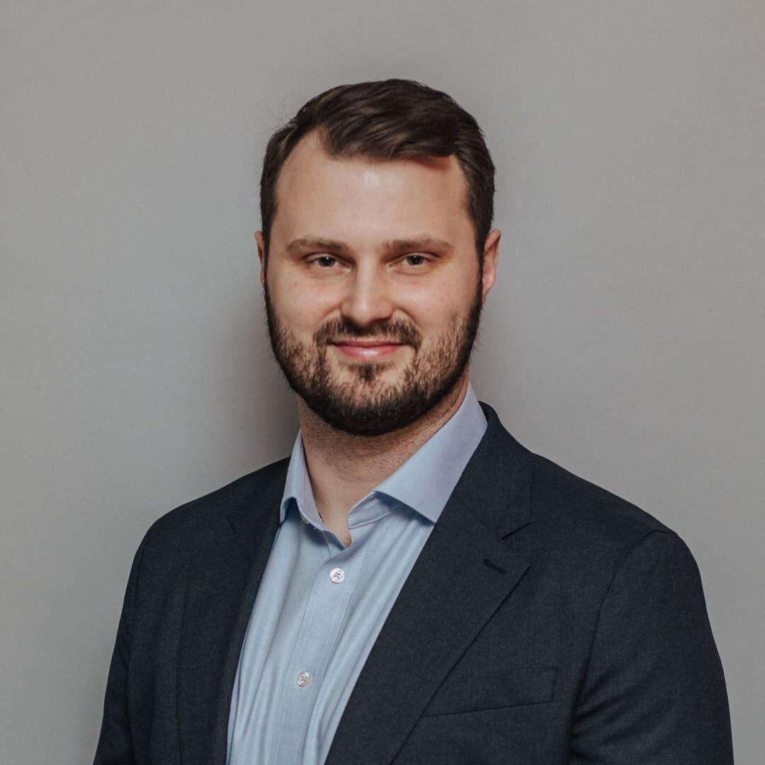 Man in a suit and blue shirt smiling.