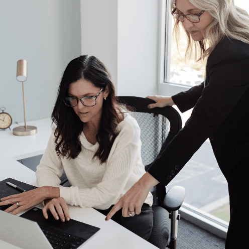 Two women working on a laptop in an office.